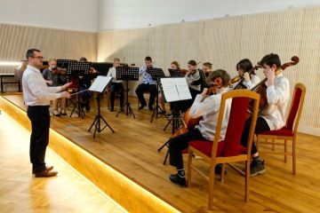 Dirigent vede žákovský smyčcový orchestr v koncertním sále