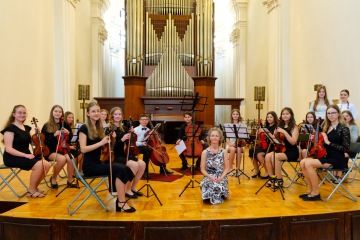 Smyčcový orchestr s vedoucí na pódiu koncertního sálu s varhanami