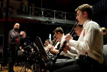 Žáci hrají na klarinety v dechovém orchestru pod vedením dirigenta